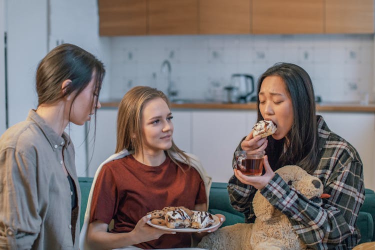 Group Of Women Sitting On A Sofa And Eating Snacks 