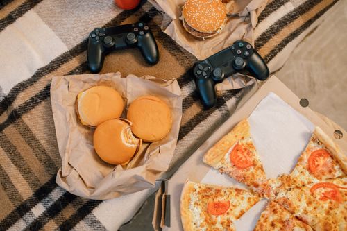 Free A top view of burgers, pizza, and gaming controllers on a soft blanket, creating a cozy atmosphere. Stock Photo