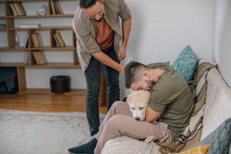 Men Cuddling Dog Sitting On Couch At Home