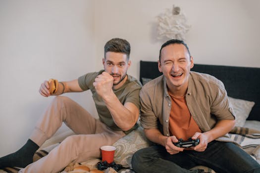 Two friends having fun playing video games indoors, sharing laughter and food.