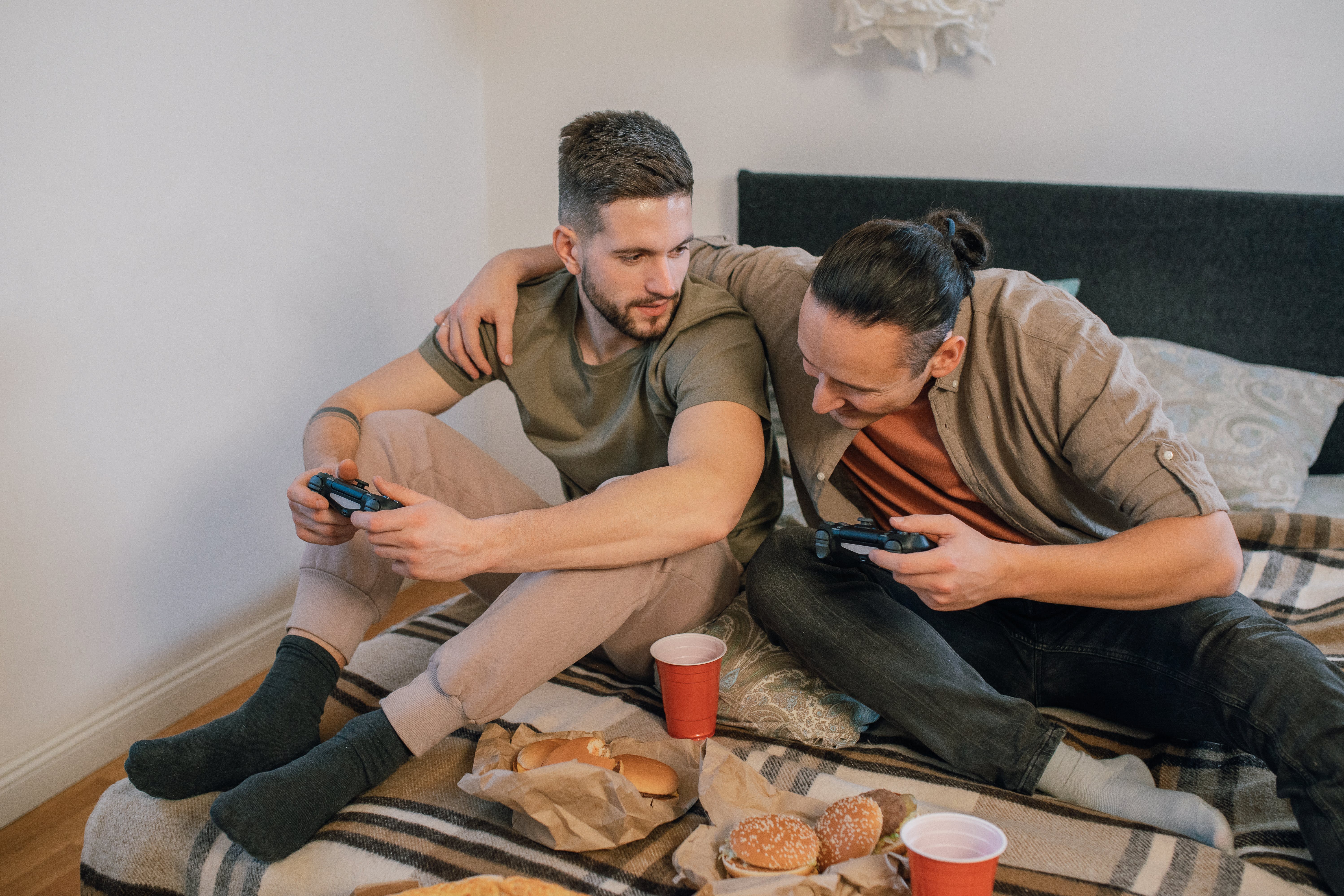 photo of men sitting on a bed while playing games together