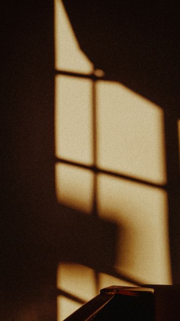 Artistic shadow cast by window frame on neutral beige wall, creating an abstract pattern.