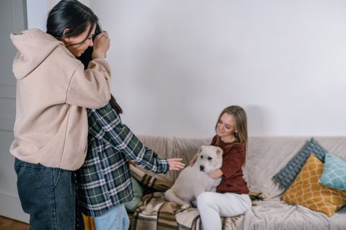 Free Three friends sitting on a couch with a white dog, enjoying a cozy moment together. Stock Photo
