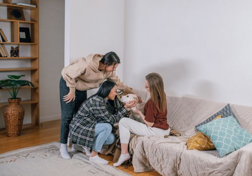 Free Three friends enjoying a relaxed moment with a dog on a couch, showcasing pet companionship. Stock Photo
