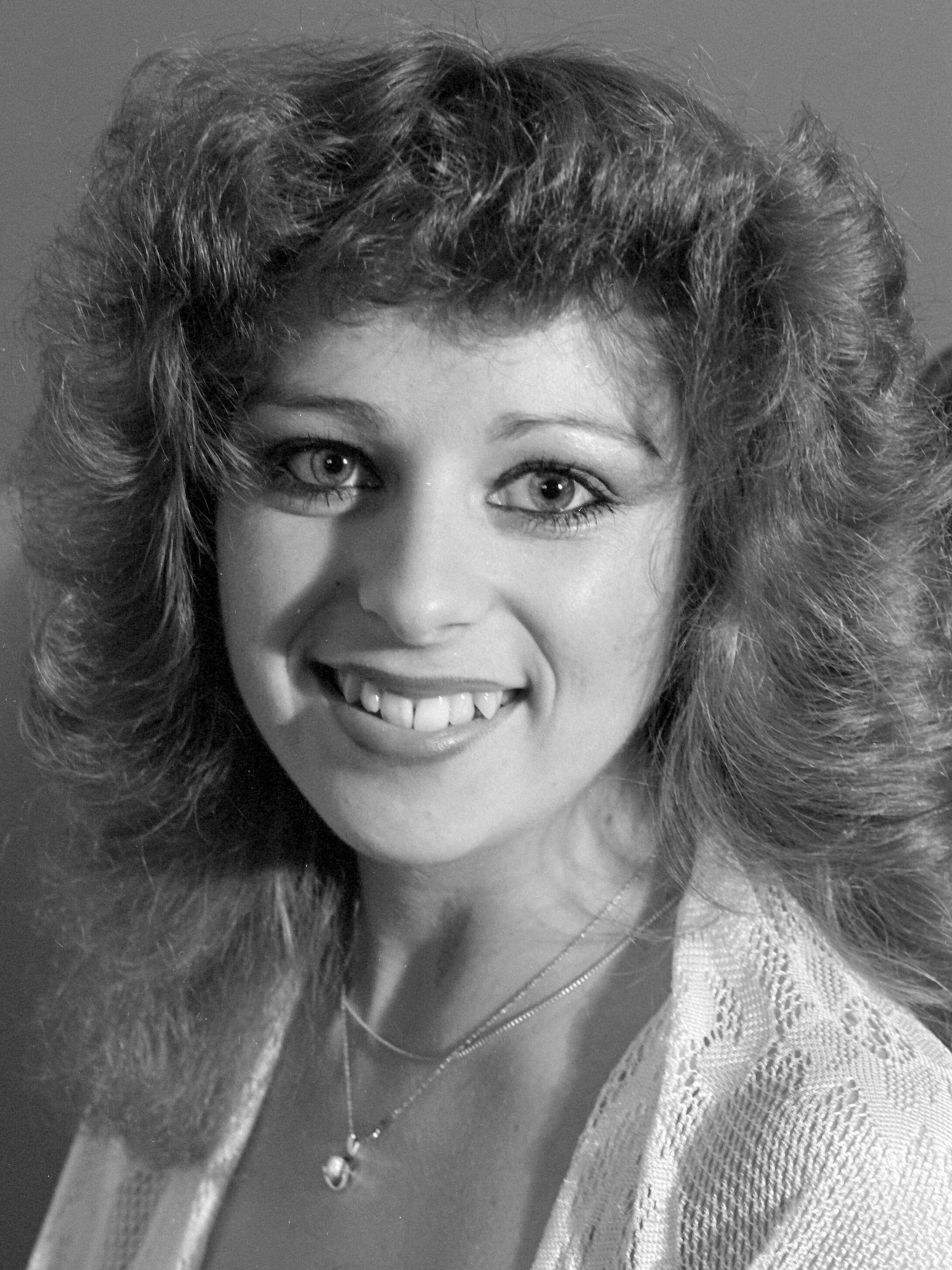 Caucasian woman with 80s hairstyle in a black and white studio portrait.