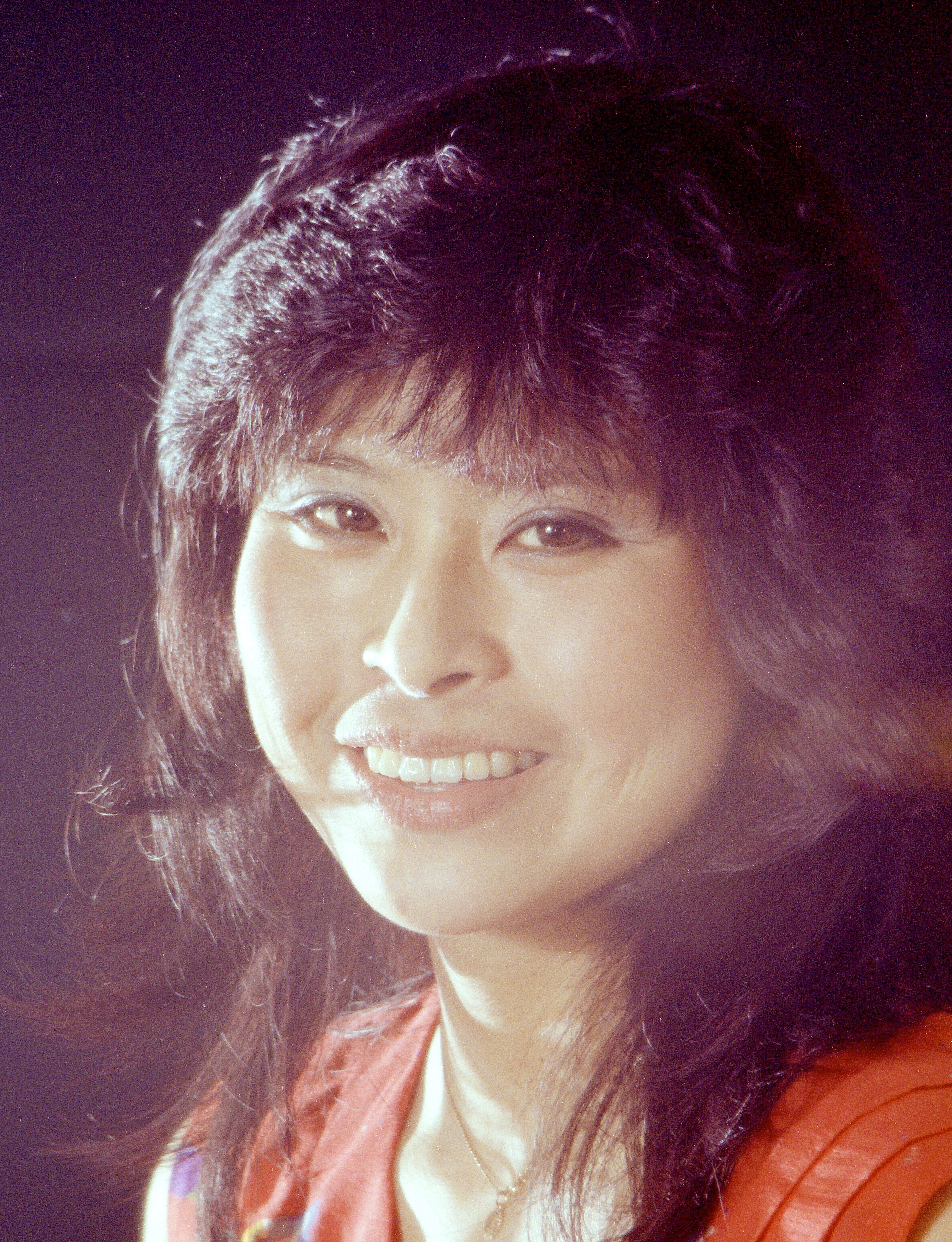 Close-up portrait of a smiling woman against a dark background in a studio setting.