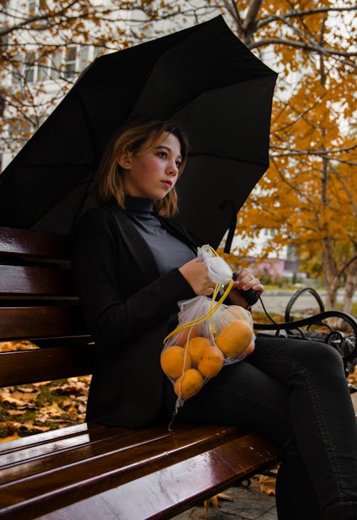 A Woman Holding a Bag of Oranges While Sitting on a Park Bench