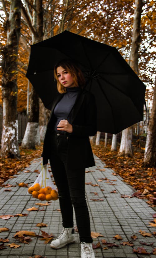 Woman Holding a Black Umbrella While Standing on the Sidewalk