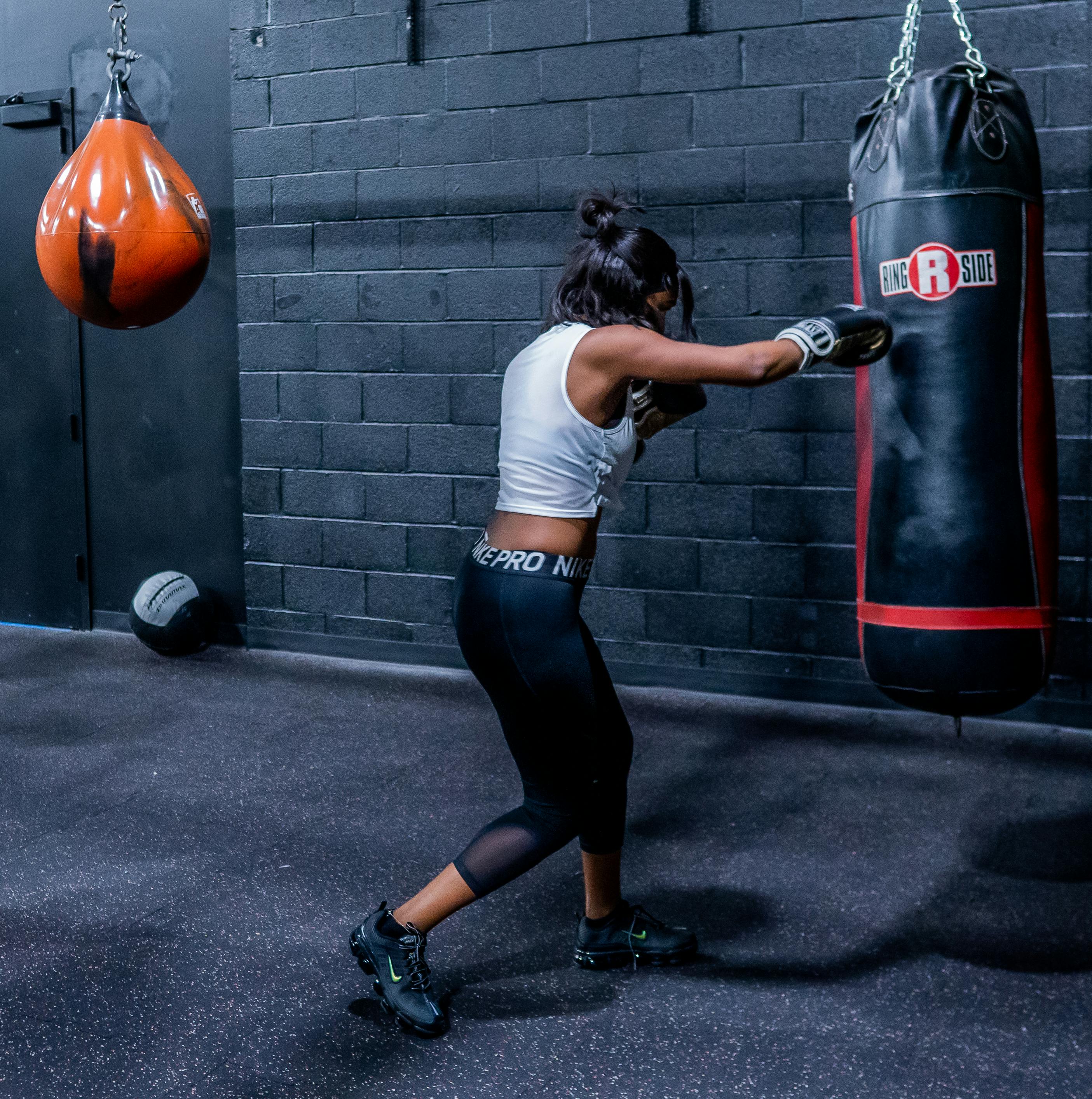 Woman in Boxing Gloves With Sports Bra Posing Boxing Style in Front of  Punching Bag · Free Stock Photo