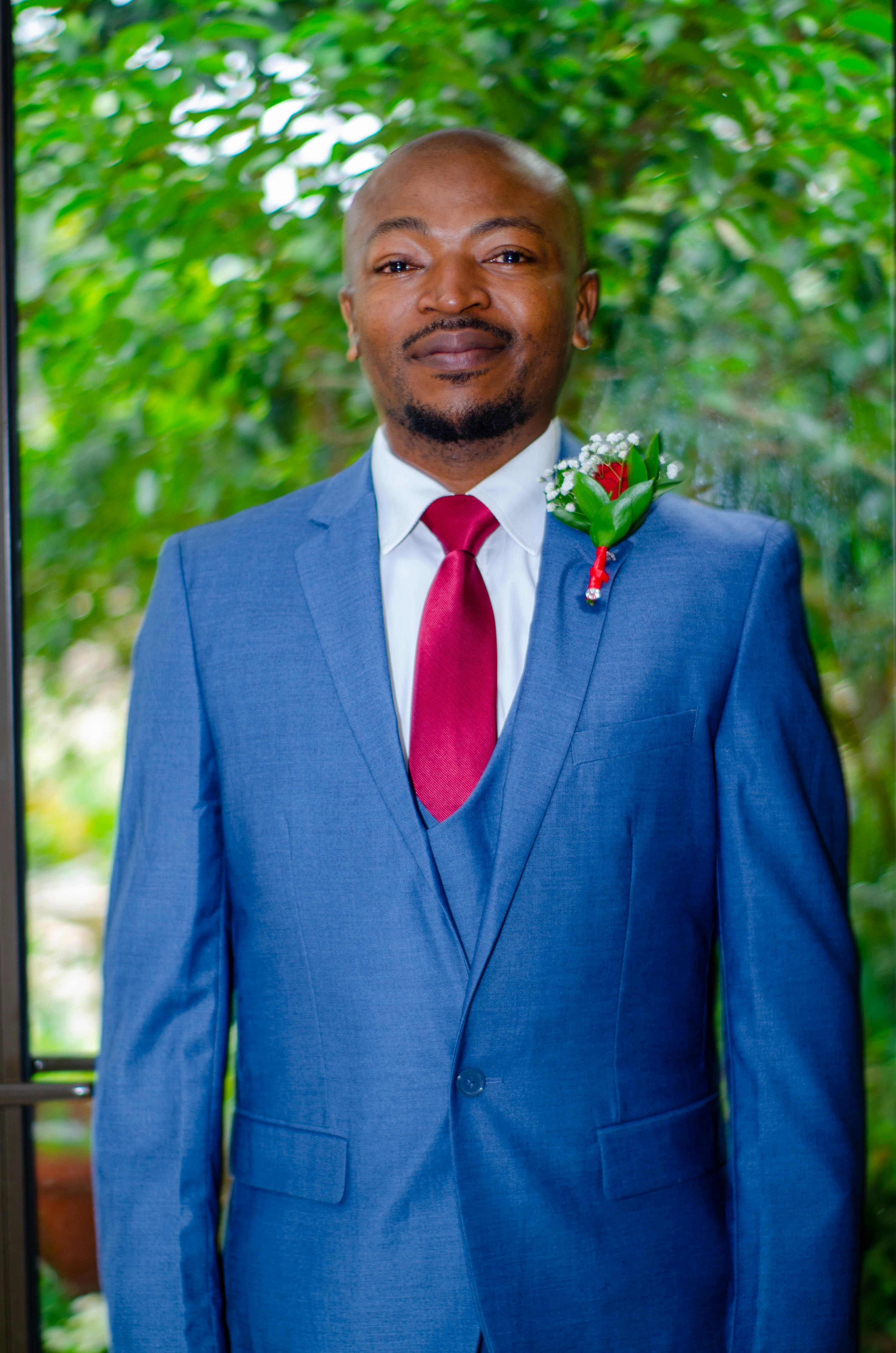 Serious African American man in formal blue suit looking at camera against green trees in daytime