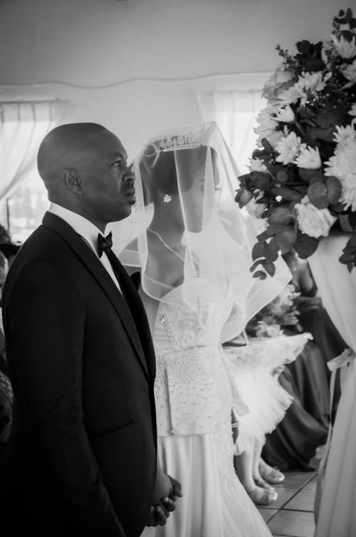 Black and white of calm African American couple in festive outfits standing together on wedding ceremony and looking forward in daytime