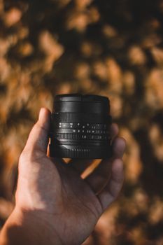 Crop unrecognizable man demonstrating digital photo camera lens with focusing and aperture rings on blurred background