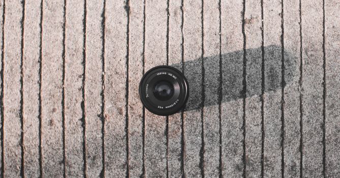 Overhead view of professional modern photo camera lens with titles on rough walkway with shadow in sunlight