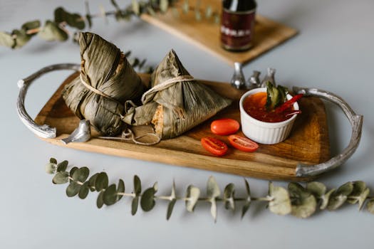 Close-up of traditional Machang with dipping sauce and cherry tomatoes on a wooden tray.