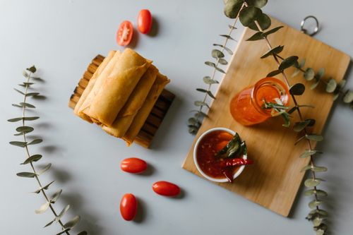 Free Top view of delicious spring rolls with sauce, cherry tomatoes, and herbs on a rustic wooden board. Stock Photo
