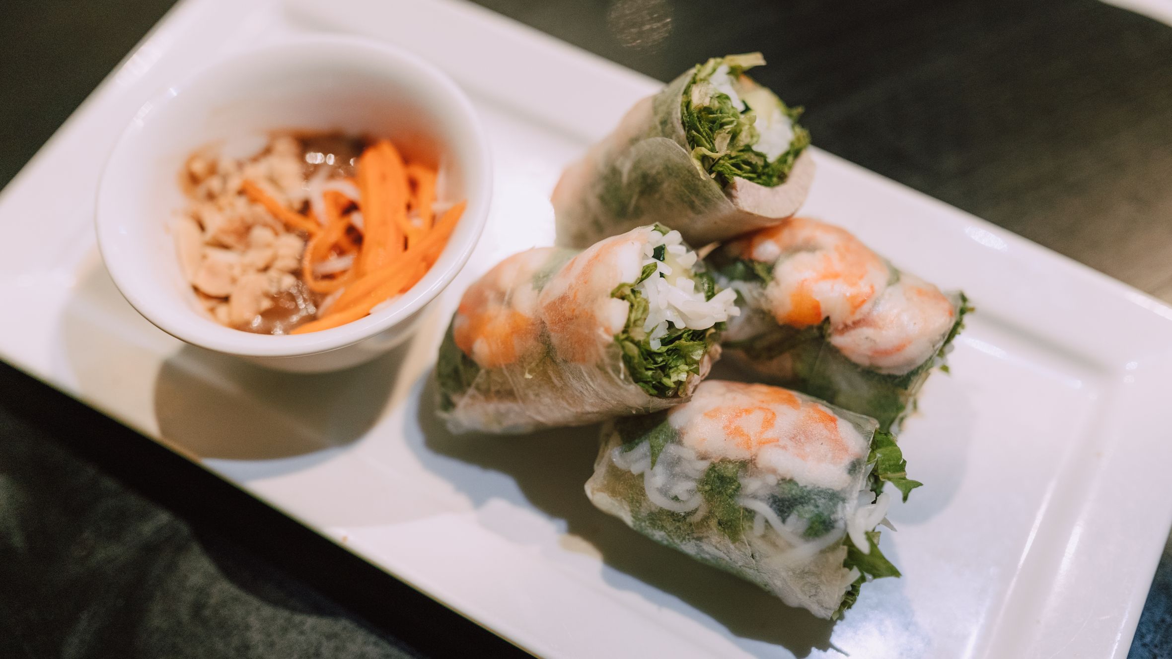 Close-up of Vietnamese spring rolls with shrimp and dipping sauce on a white plate.