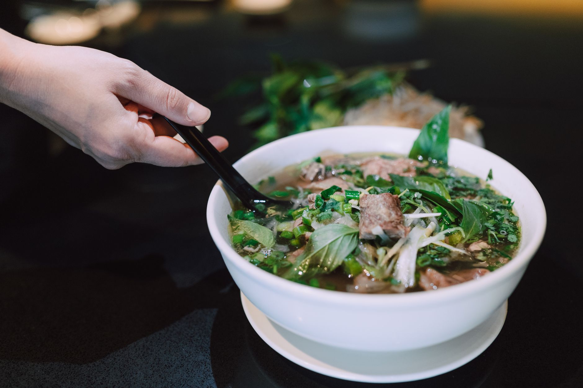 Close-up of a hand holding chopsticks over a bowl of flavorful Vietnamese pho.