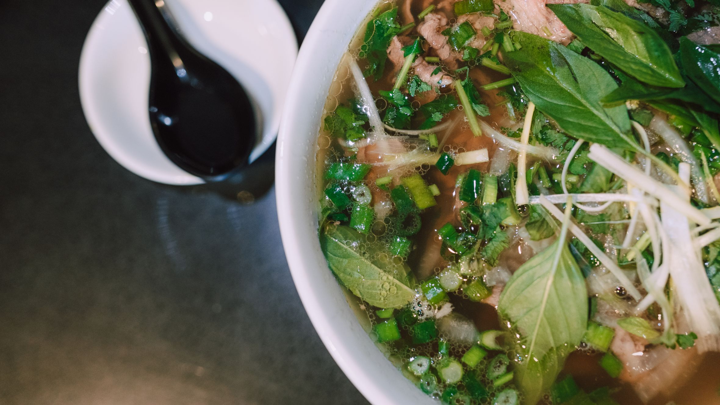Delicious, traditional Vietnamese pho soup with fresh herbs and toppings in a white bowl.
