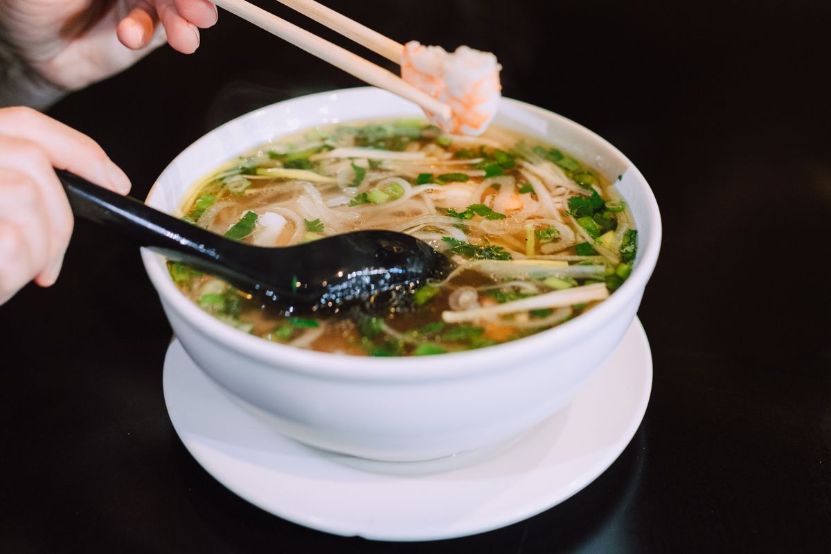 Chopsticks lifting rice noodles from a bowl of pho