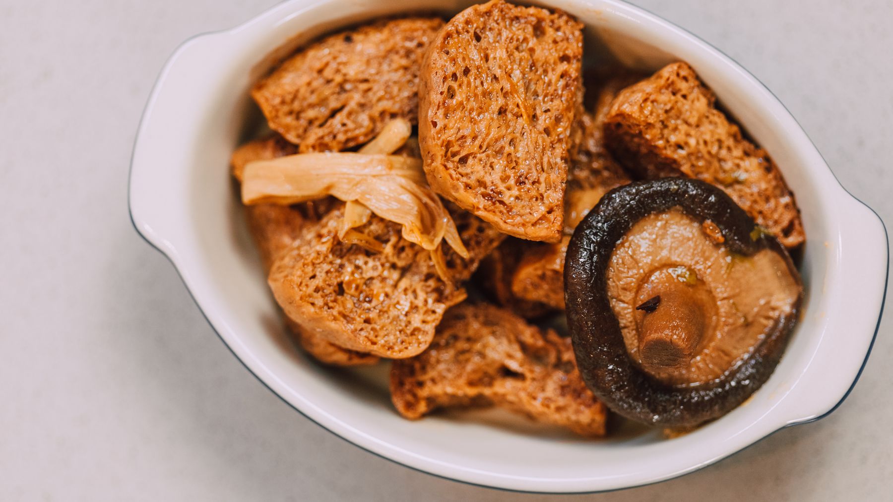 Close-up of traditional Asian tofu dish with mushrooms in a white bowl, showcasing delicious food presentation.
