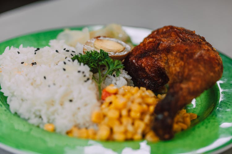 A Plate Of Fried Chicken And Rice With Corn On The Side