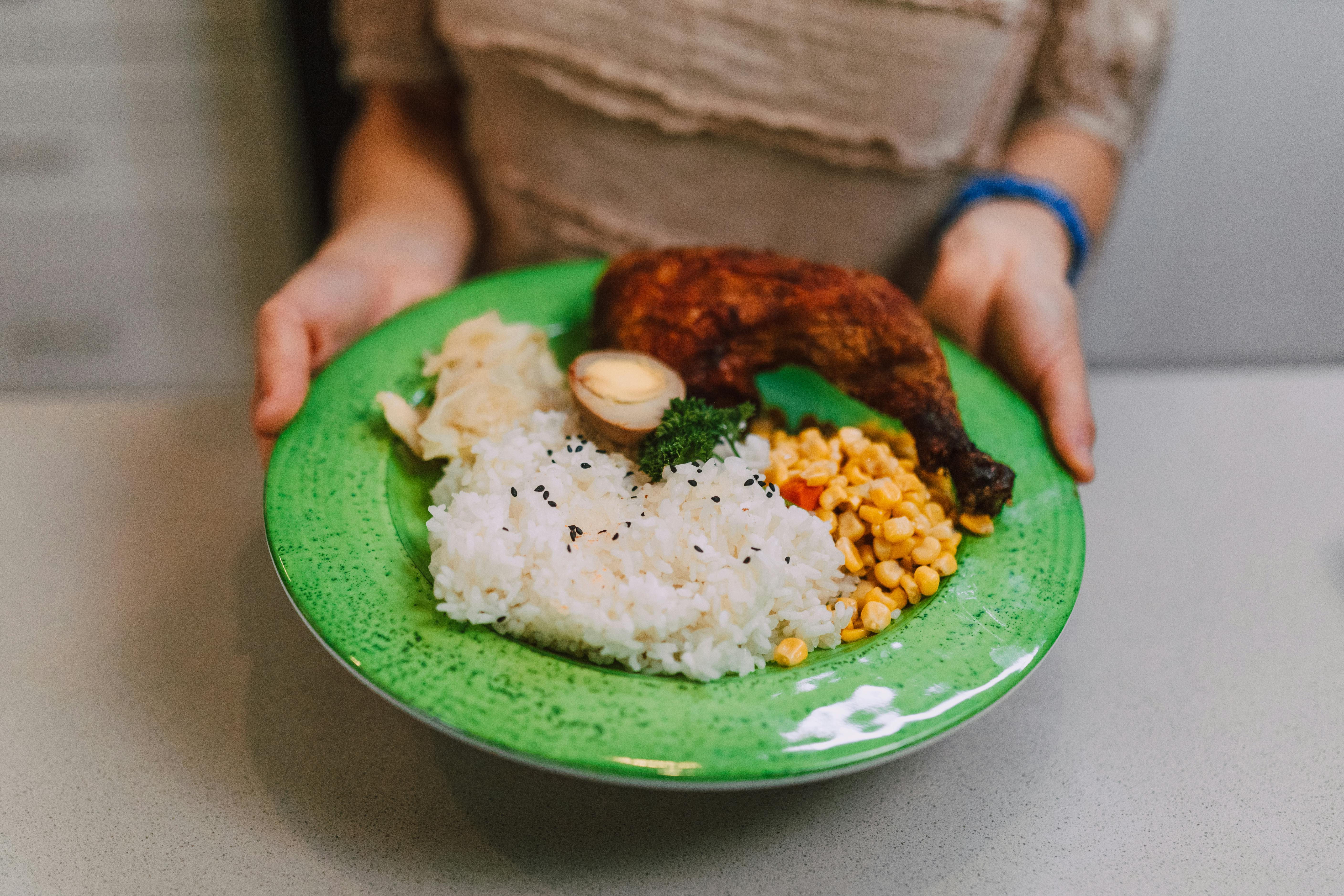 A colorful dish featuring rice, chicken, corn, and garnish served on a green plate.