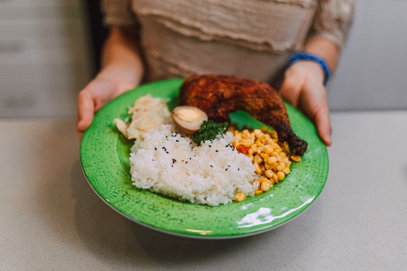 A colorful dish featuring rice, chicken, corn, and garnish served on a green plate.
