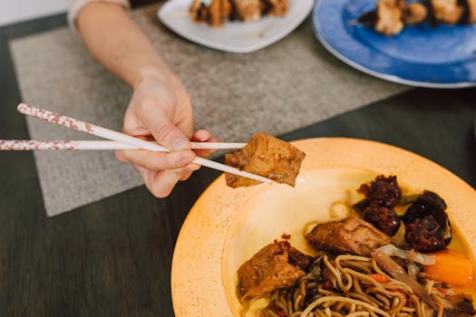 Plate of Asian cuisine featuring tofu and noodles, captured with chopsticks for an authentic feel.
