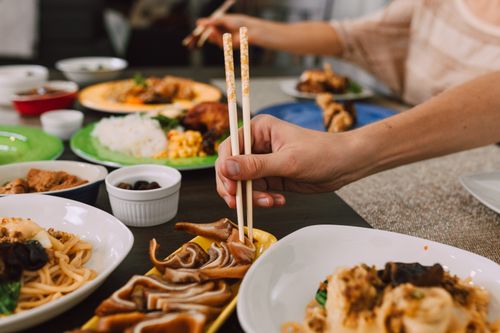 Free Close-up of hands using chopsticks to enjoy a variety of Asian dishes at a dining table. Stock Photo