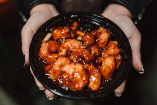 Close-up of a person holding a bowl of delicious Asian chicken dish in orange sauce.