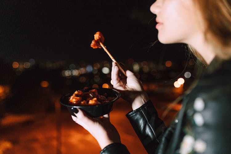 Close-up Shot Of A Woman Eating Meat With Orange Sauce