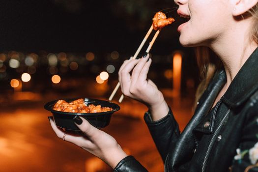 Close-up of a woman using chopsticks to eat food in a nighttime setting.