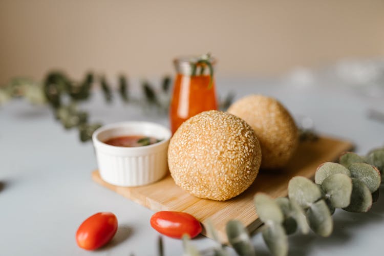 Sesame Balls Beside Ramekin With Orange Dip On A Wooden Chopping Board