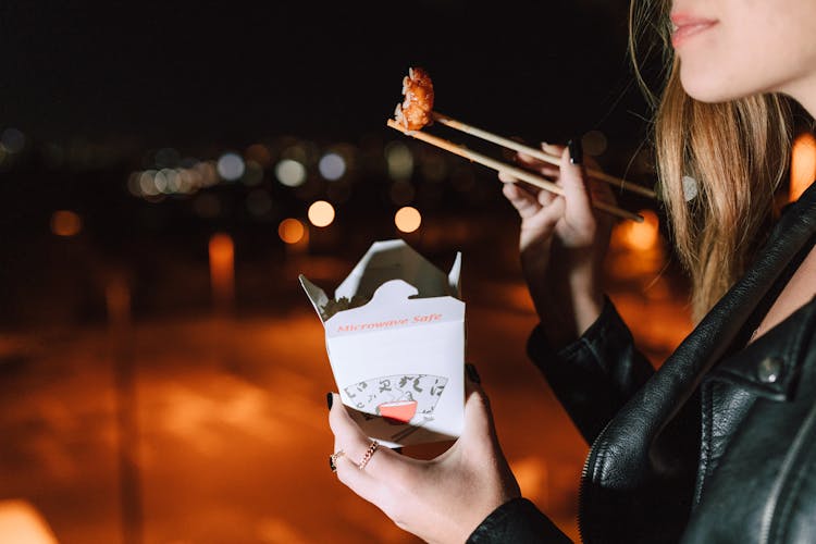 Woman In Black Jacket Eating Takeaway Food