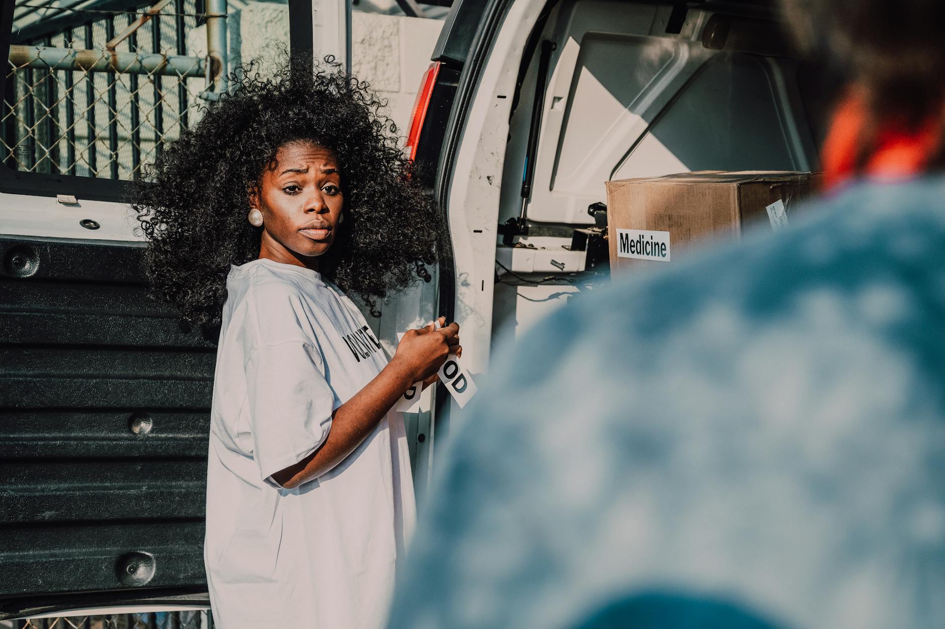 A woman assists with unloading medicine boxes from a van for a community charity event.