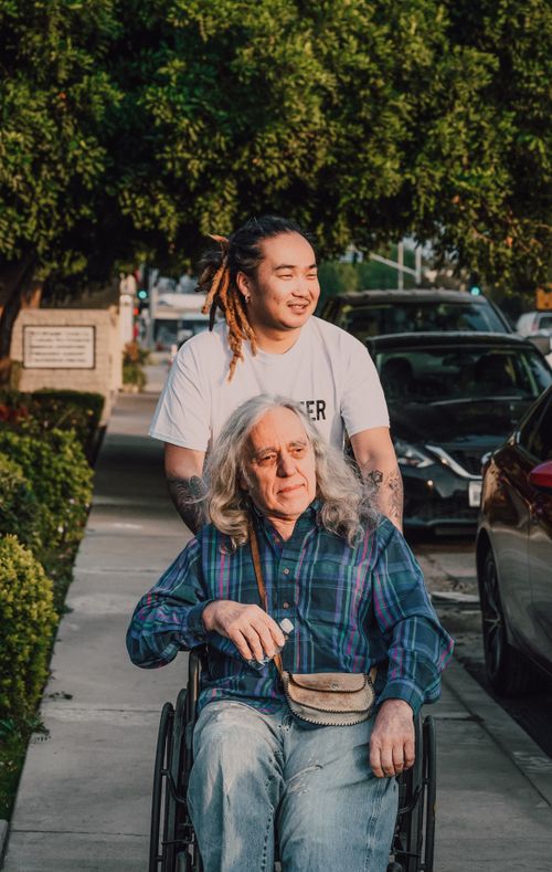 Free A young man pushes an elderly man in a wheelchair on a sunny sidewalk. Stock Photo