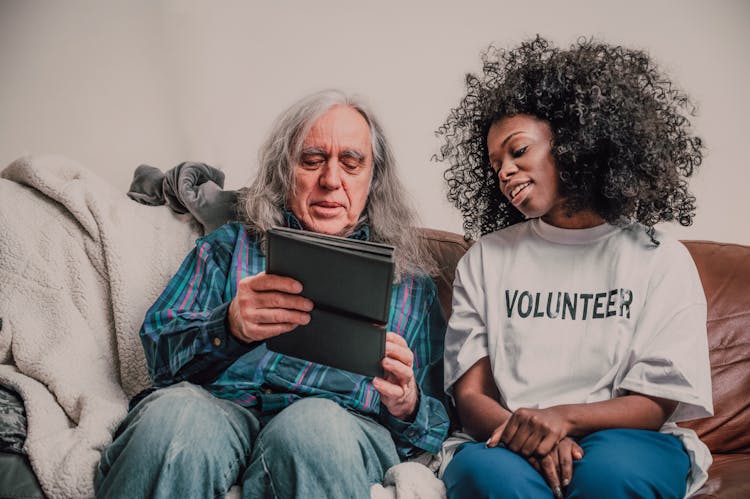 A Woman Wearing Volunteer Shirt Sitting Beside Elderly Man Holding Tablet Computer