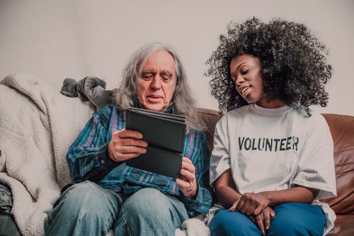 Free Young volunteer helps senior man with technology, fostering connection indoors. Stock Photo