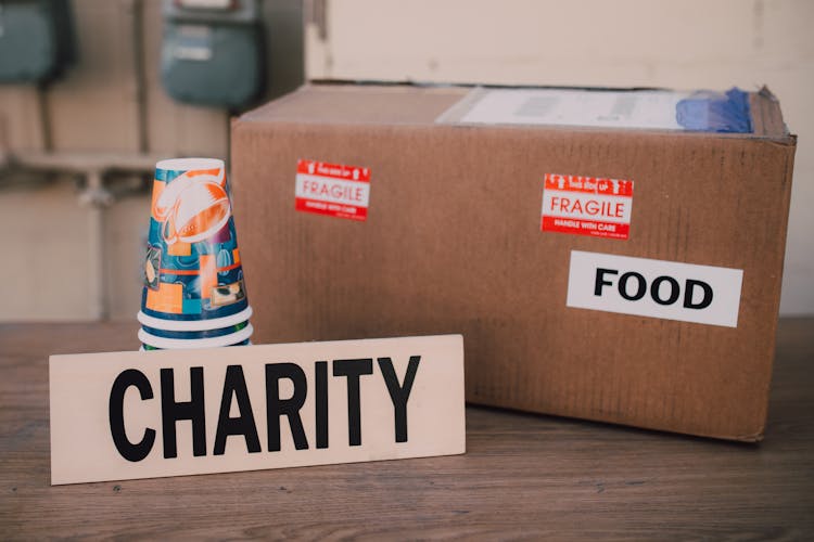 A Cardboard Box With Food Label Beside A Charity Sign And Paper Cups