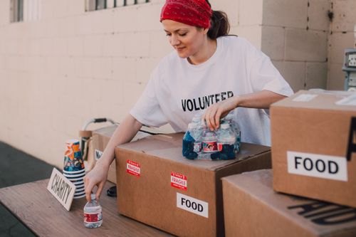 Free Woman volunteer sorting food and water for charity distribution at aid center. Stock Photo