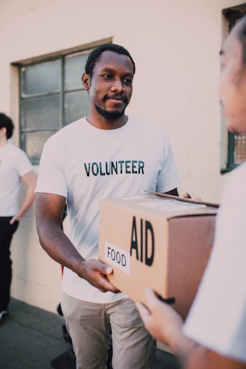 Man in White Crew Neck T-shirt Holding Brown Box