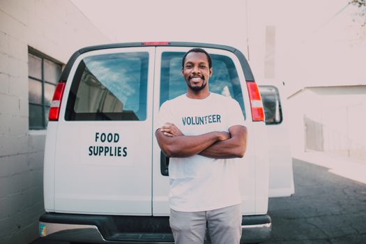 Male volunteer standing confidently in front of a food delivery van.