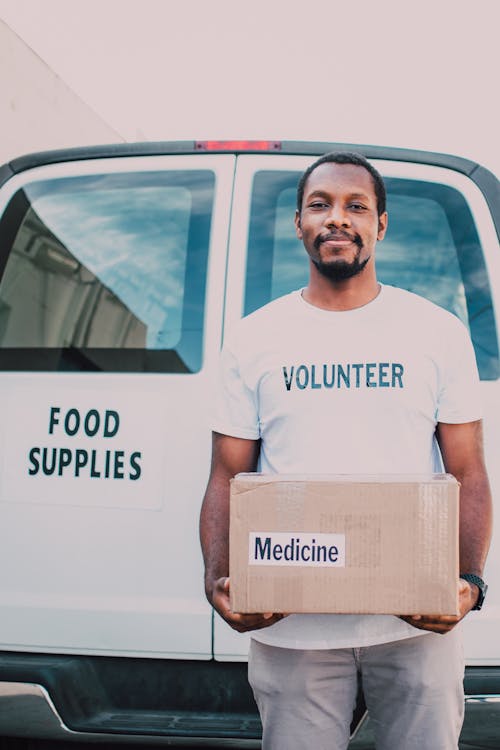 A Man Standing Beside the White Van Holding a Box 