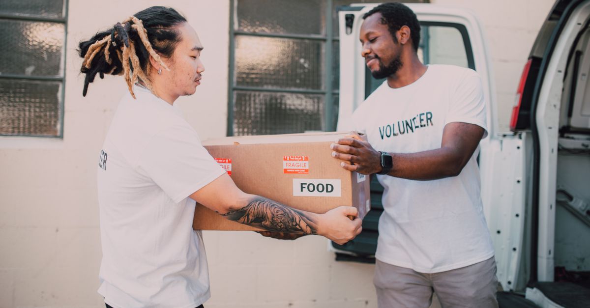 Two volunteers transferring a food box from a van, symbolizing community support and charity work.