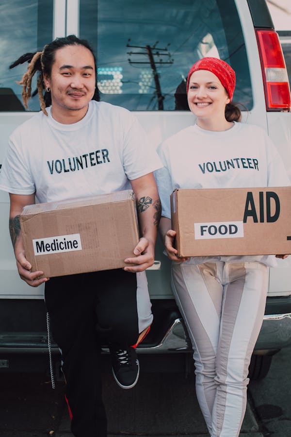 Man and Woman Carrying Medicine and Food Labelled Cardboard Boxes Behind a White Van