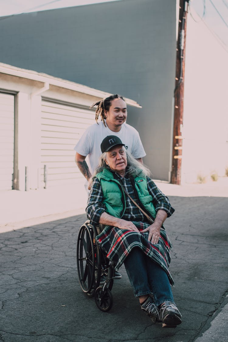 Man Pushing An Elderly Man On A Black Wheelchair