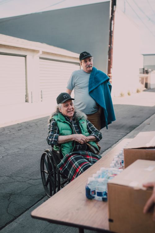 Free A heartwarming moment as volunteers distribute essentials to an elderly man in a wheelchair outdoors. Stock Photo