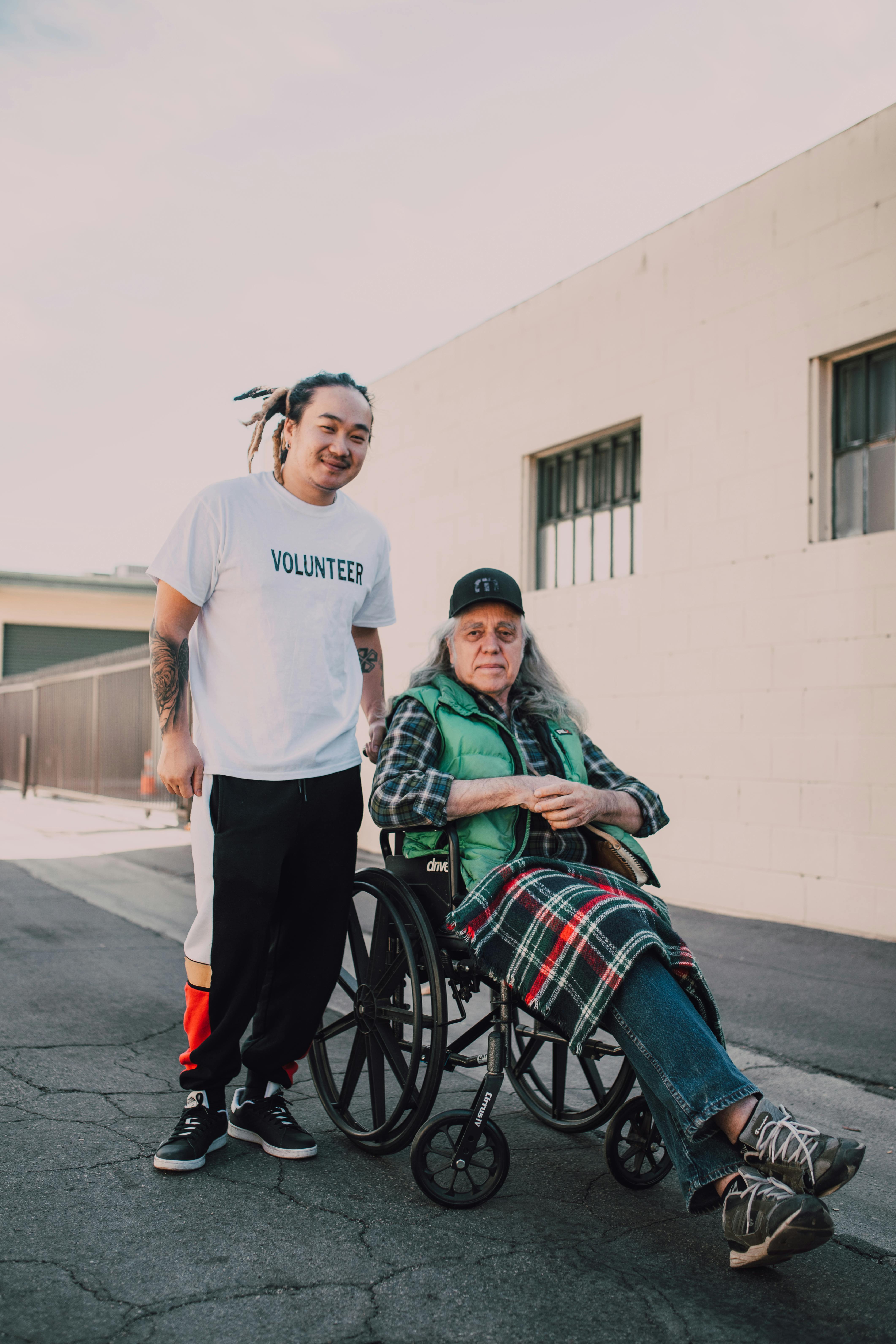 a tattooed volunteer beside a man in a wheelchair