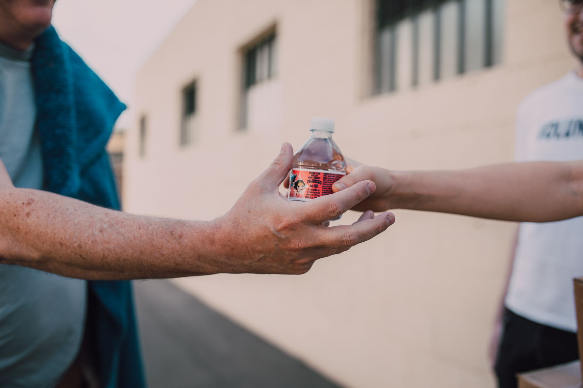 Two people exchanging a bottle outdoors, emphasizing connection and kindness.