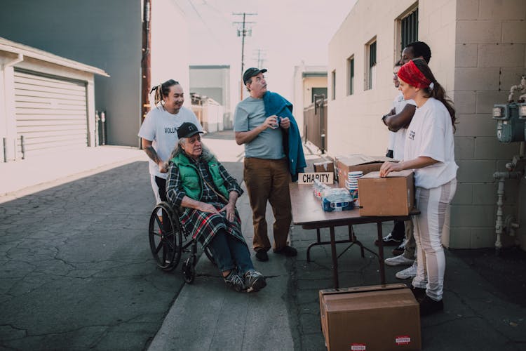 Elderly Man In A Wheelchair Talking To A Group Of Volunteers